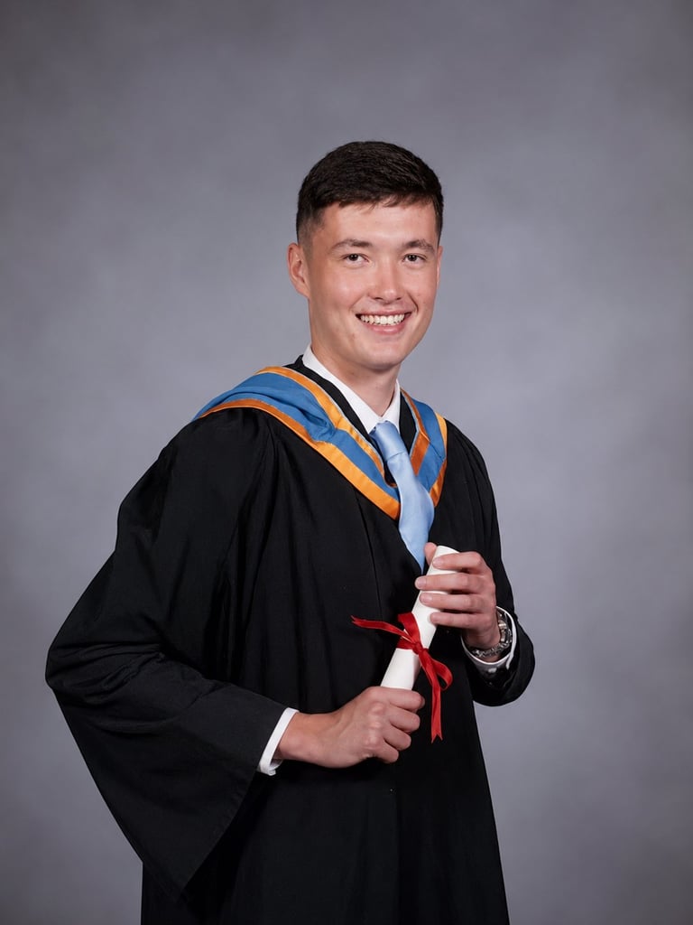 Young man in black graduation gown and blue-gold regalia holding a red diploma, smiling at camera